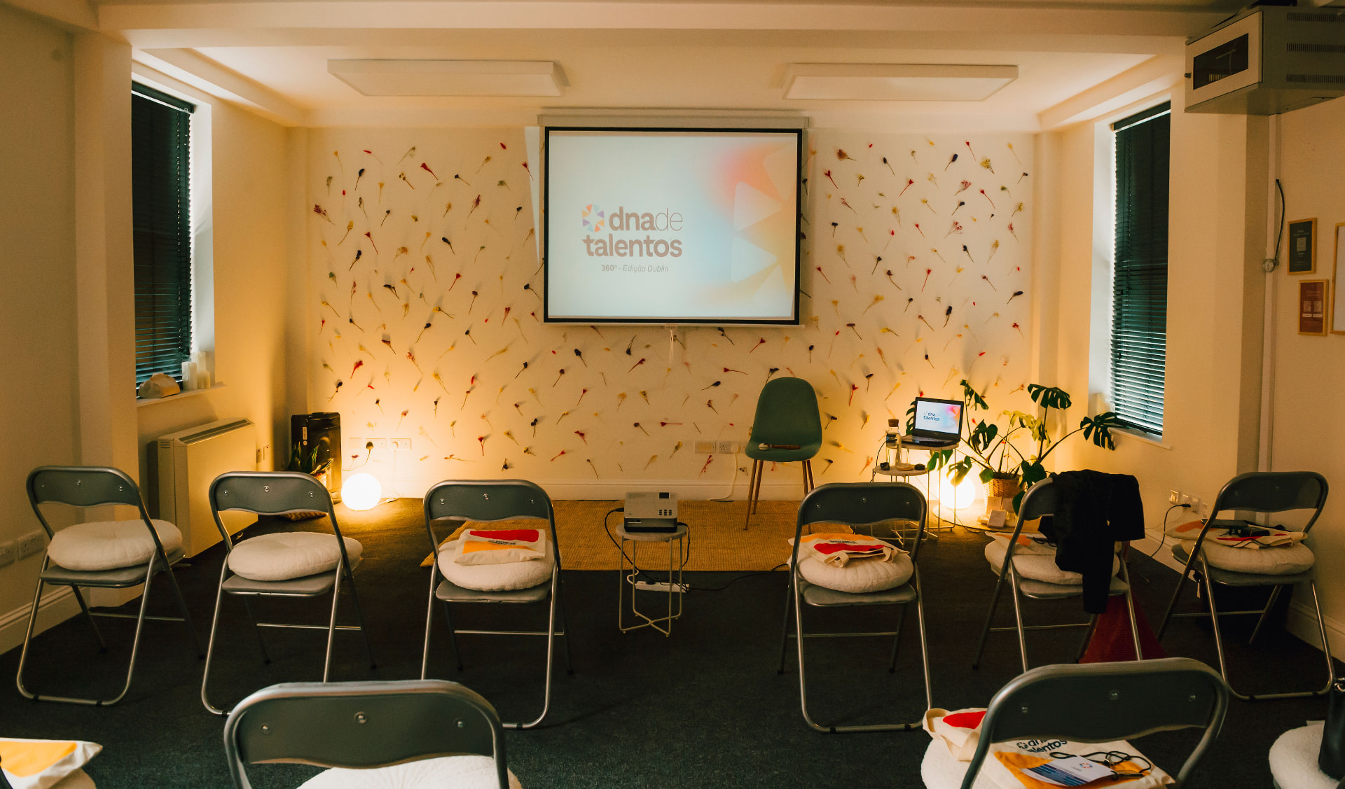 Anú Room set up in a circle of chairs facing a screen, with a dried-flower wall