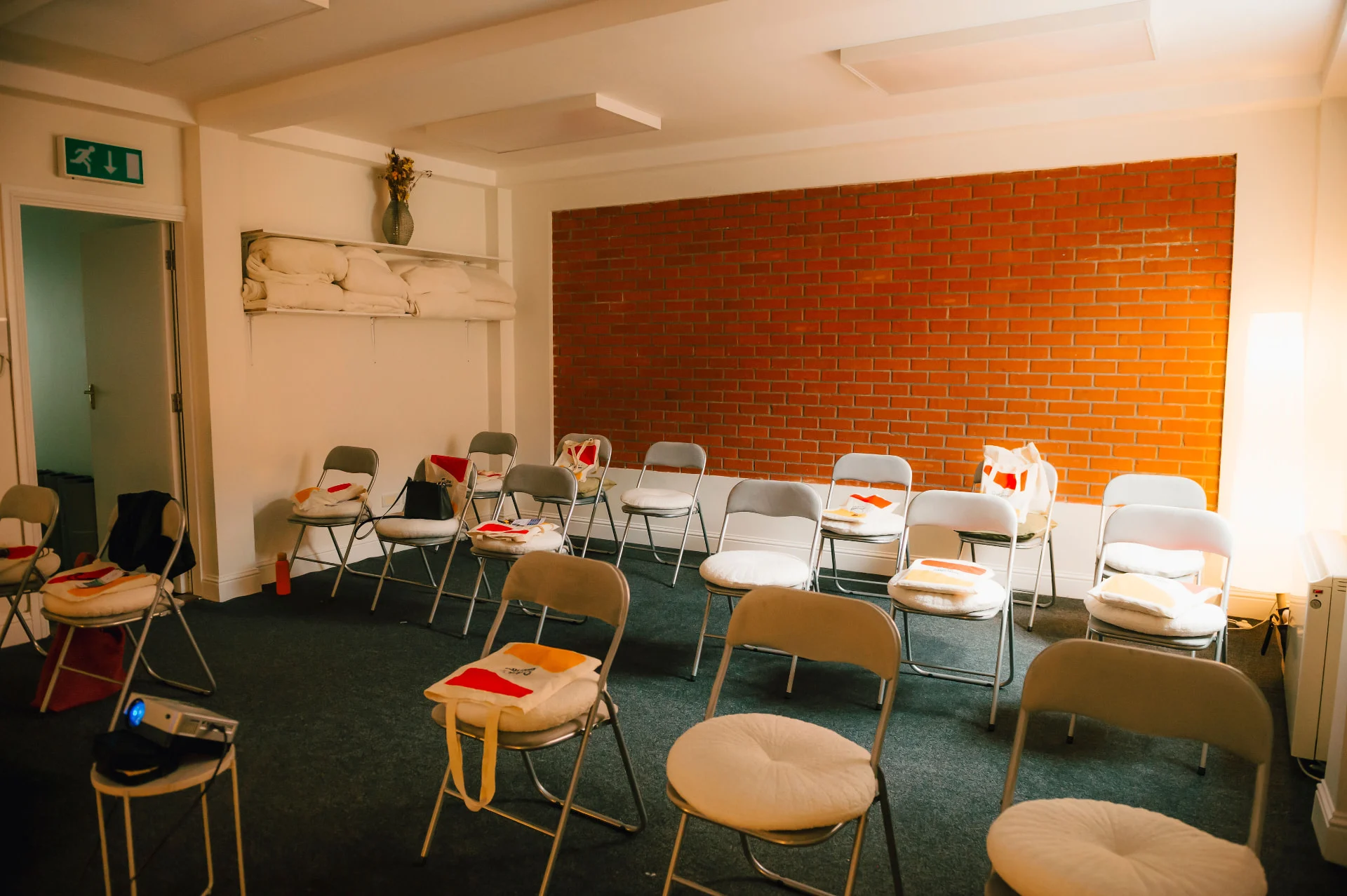 Anú Room arranged theatre style with cushioned chairs beside a brick feature wall